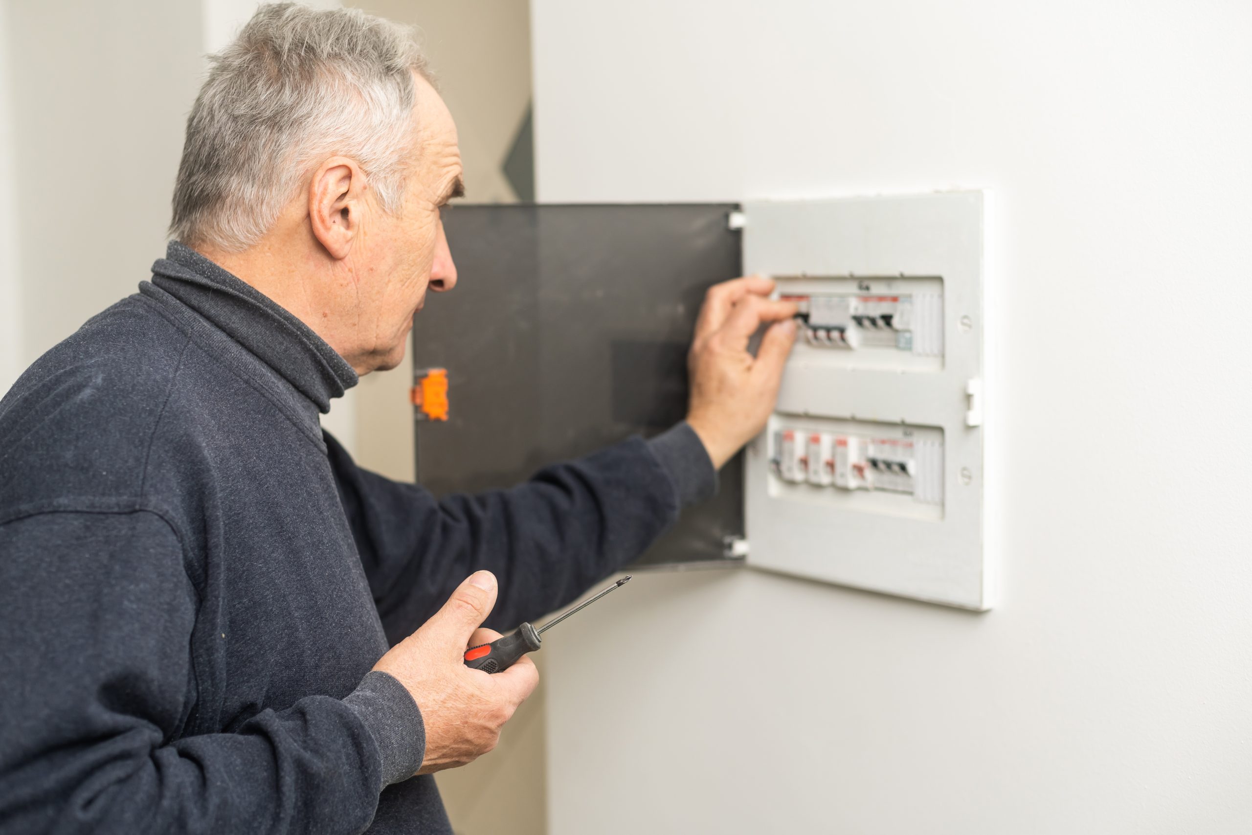 Mature man an electrician turning on circuit breaker in panel.