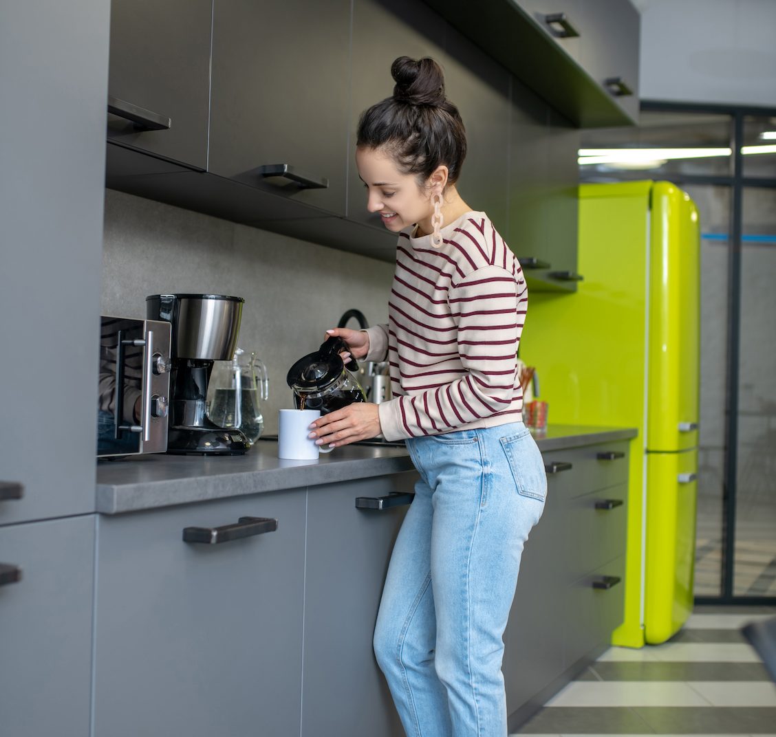 Young woman pouring coffee into white cup